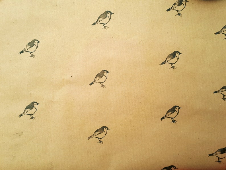 May include: Tan-colored paper with a repeating pattern of small, stylized birds. Each bird is depicted in black and white, with a simple, illustrative style. The birds are evenly spaced across the surface.