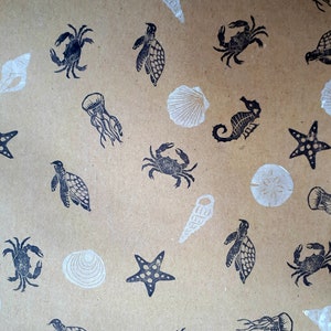 May include: A brown paper gift wrap with a repeating pattern of black sea creatures and white seashells. The pattern includes starfish, seahorses, crabs, turtles, and jellyfish.