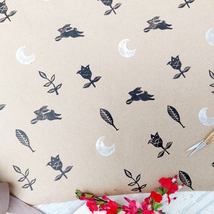 May include: Brown paper gift wrap with a repeating pattern of black silhouettes of rabbits, flowers, leaves, and crescent moons.