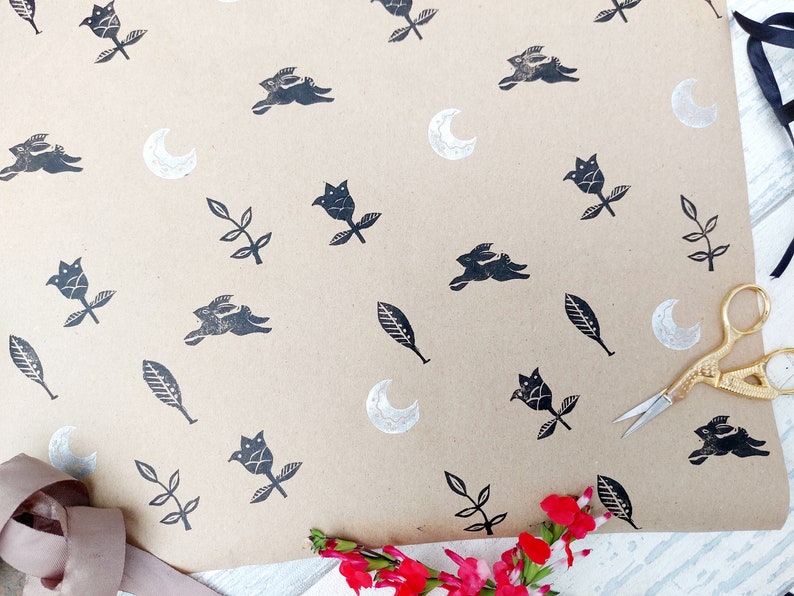 May include: Brown paper gift wrap with a repeating pattern of black silhouettes of rabbits, flowers, leaves, and crescent moons.