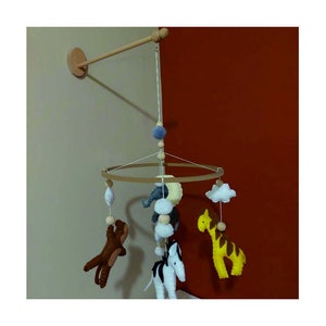 May include: A wooden mobile with felt animal toys hanging from a circular wooden frame. The animals include a zebra, giraffe, elephant, and a brown animal. The mobile is suspended from a wooden arm attached to the wall.