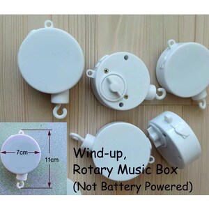 May include: Five white wind-up music boxes with a hook for hanging. The music boxes are 7 cm in diameter and 11 cm tall. The text on the image reads "Wind-up, Rotary Music Box (Not Battery Powered)".