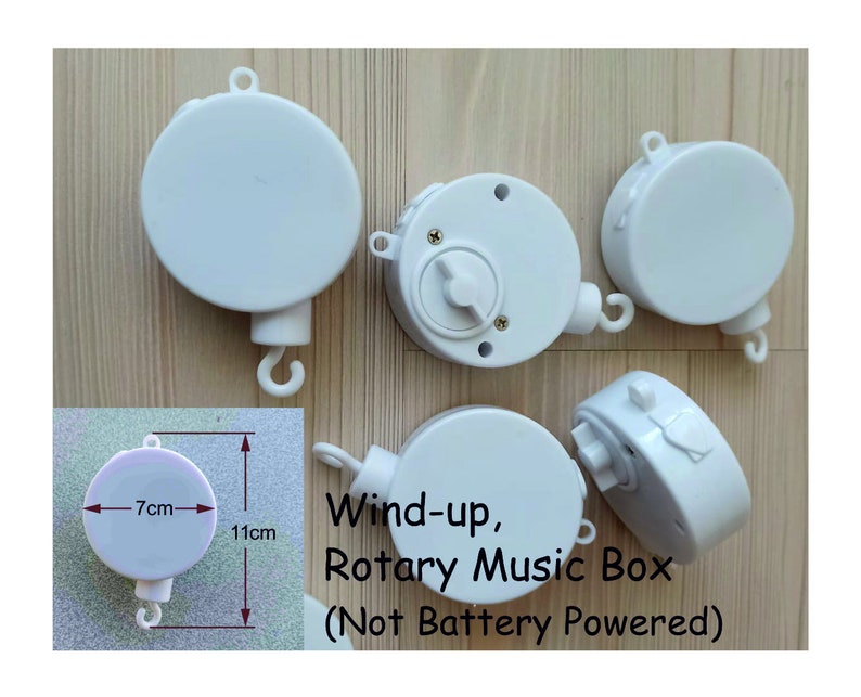 May include: Five white wind-up music boxes with a hook for hanging. The music boxes are 7 cm in diameter and 11 cm tall. The text on the image reads "Wind-up, Rotary Music Box (Not Battery Powered)".