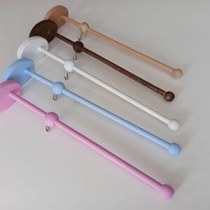 May include: Five wooden mobile holders in different colors: pink, light blue, white, brown, and beige. Each holder has a round base and a long, thin rod with a ball at the end.