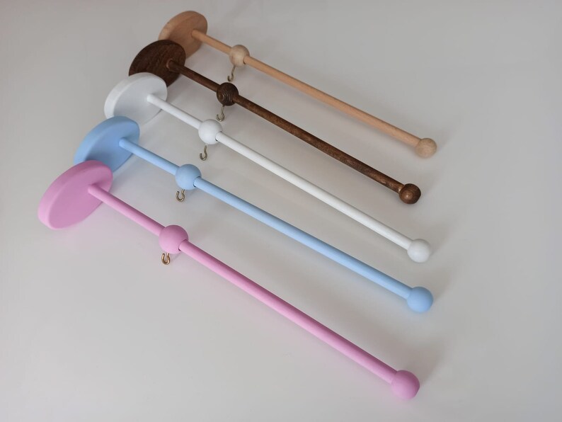 May include: Five wooden mobile holders in different colors: pink, light blue, white, brown, and beige. Each holder has a round base and a long, thin rod with a ball at the end.