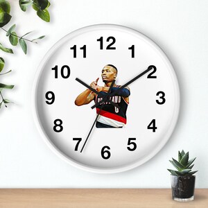 May include: White wall clock with black numbers and hands. The clock features a basketball player in a red and black jersey with the number 0 on the front. The player is in a shooting pose.