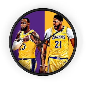 May include: A black and yellow wall clock featuring a cartoon illustration of two basketball players wearing Los Angeles Lakers jerseys. The player on the left is wearing jersey number 23 and the player on the right is wearing jersey number 21.