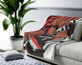 May include: A white fleece blanket with a black and white striped pattern. A basketball player in a red, black, and white jersey is featured on the blanket. The player is pointing with his right hand. The text "Rip City" is visible on the jersey.