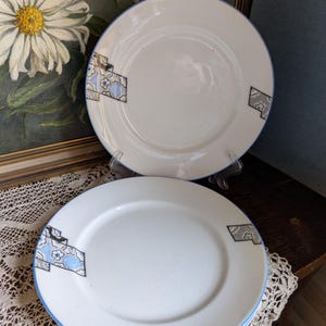 Puede incluir: Tres platos de cena de cerámica blanca con un diseño geométrico azul y gris. Los platos tienen un borde azul y una textura sutilmente moteada.