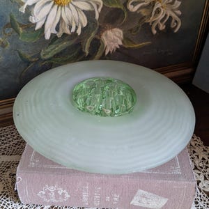 Könnte beinhalten: Eine gefrostete Glasschale mit einem grünen Glaseinsatz. Die Schale hat ein geriffeltes Design und steht auf einem Buch.