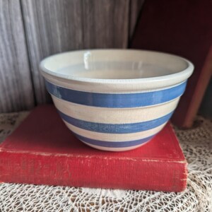 Può includere: Una ciotola per mescolare in ceramica vintage con base color crema e strisce blu. La ciotola è appoggiata su un libro rosso. La ciotola ha un design classico, ideale per la cucina o l'esposizione. Diametro circa 20 cm.