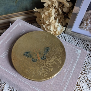Bonito polvo compacto vintage en tono dorado con mariposa azul.