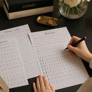 May include: Three white practice sheets with black printed calligraphy exercises featuring the headings Pressure control, Uppercases, and Lowercases. The sheets contain rows of repeating letters and strokes for handwriting practice on a dark surface.