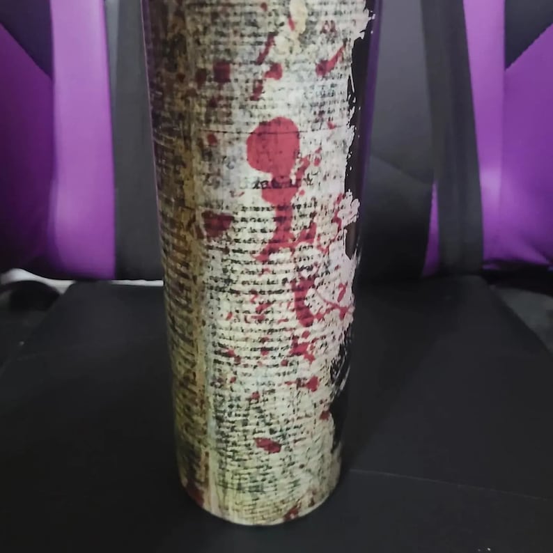 Puede incluir: Un vaso negro y blanco con un dise&ntilde;o de p&aacute;gina de libro vintage y salpicaduras de pintura roja.