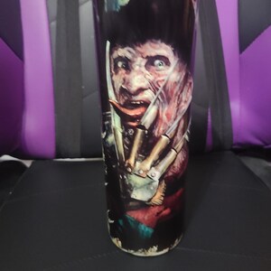 Puede incluir: Un vaso de acero inoxidable negro y rojo con un gr&aacute;fico de un personaje de pel&iacute;cula de terror con un cuchillo. El personaje tiene una m&aacute;scara blanca y lleva un sombrero marr&oacute;n.