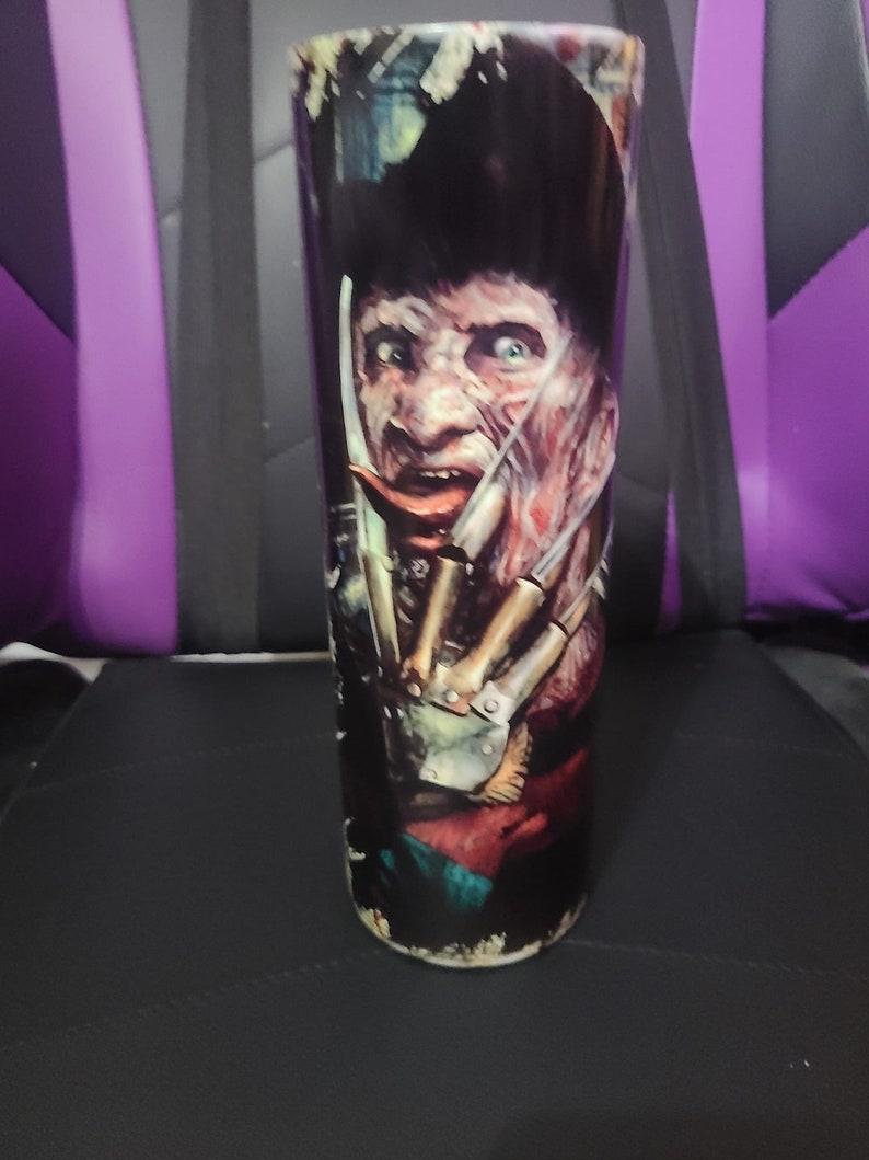 Puede incluir: Un vaso de acero inoxidable negro y rojo con un gr&aacute;fico de un personaje de pel&iacute;cula de terror con un cuchillo. El personaje tiene una m&aacute;scara blanca y lleva un sombrero marr&oacute;n.