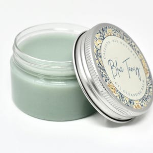 May include: A glass jar with a silver lid containing a light blue cleansing balm. The lid has a floral design and the text "Callista All Natural Blue Tangy Oil Cleansing Balm".