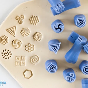 May include: A set of 16 silicone stamps featuring a variety of geometric and abstract designs. The stamps are arranged in a grid on a white surface. The text "Texturio Stamps" is visible in the bottom left corner of the image.