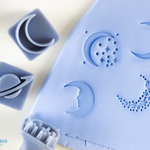 Könnte beinhalten: Ein Satz von fünf blauen Gummistempeln mit verschiedenen Mond- und Sternmotiven. Die Stempel befinden sich auf einer hellblauen Oberfläche. Der Text "Texturio Stamps" ist in der linken unteren Ecke des Bildes sichtbar.