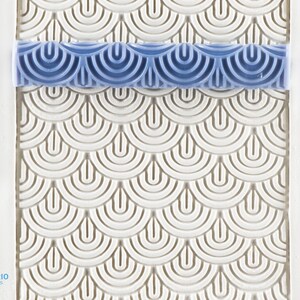 May include: A blue and white textured roller for creating a decorative pattern on fondant or clay. The roller has a repeating pattern of overlapping half circles.