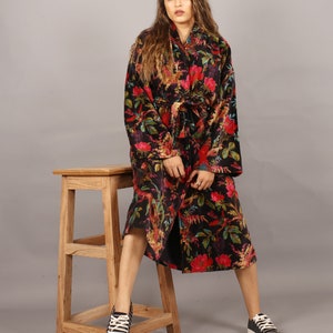 May include: A black floral print long-sleeved robe with a tie belt. The robe is worn by a person with long brown hair and is sitting on a wooden stool.