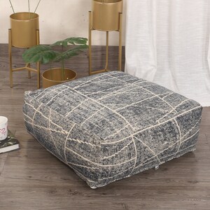 May include: A square, gray and white patterned ottoman with a zipper closure. The ottoman is sitting on a wooden floor.
