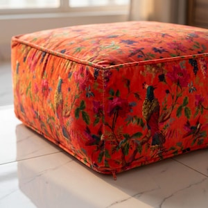 Peut inclure: Un coussin de sol carré recouvert d'un tissu en velours orange vif. Le matériau présente un imprimé botanique et aviaire détaillé, mettant en scène des oiseaux colorés perchés parmi des fleurs épanouies et un feuillage vert, avec des bords passepoilés.