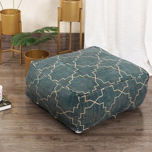 May include: A square, teal blue and gold patterned floor cushion with a geometric design. The cushion is sitting on a wooden floor.