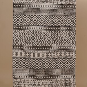 Op de afbeelding: Zwart-wit geometrisch tapijt met franjes aan de uiteinden. Het tapijt heeft een verscheidenheid aan verschillende patronen, waaronder ruiten, vierkanten en spiralen.