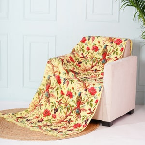 May include: A yellow throw blanket with a floral and bird pattern. The blanket is draped over a white armchair.
