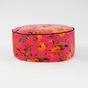 May include: A round pink velvet ottoman with a black trim and a floral print featuring birds and flowers.