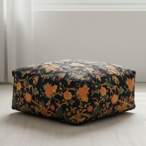 May include: Square ottoman with a dark navy background and a floral pattern in shades of orange, yellow, and green. The ottoman is a low, square shape, suitable for use as a footrest or extra seating.