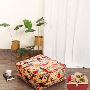 May include: A square, cream-colored floor cushion with a floral and bird print. The cushion has a zipper closure and is filled with a soft, comfortable material. The cushion is sitting on a wooden floor.