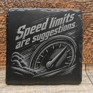 May include: A square black slate coaster with rough, uneven edges. The surface features an engraved graphic of a speedometer with motion lines and smoke, accompanied by the text "Speed limits are suggestions" in a bold, slanted font.