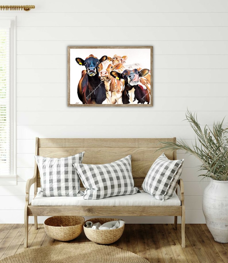 May include: A framed watercolor painting of four cows with brown and white markings. The cows are looking directly at the viewer with their tongues sticking out. The painting is set against a white background.