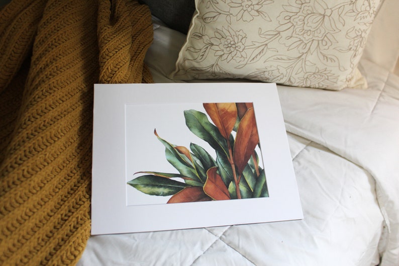 May include: A framed watercolor painting of a cluster of green and orange leaves. The leaves are arranged in a loose, organic pattern, and the colors are vibrant and realistic.