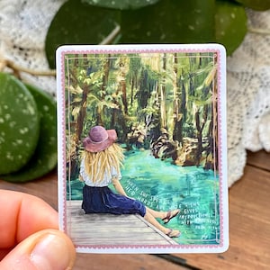 May include: A sticker featuring an illustration of a person sitting on a dock, looking at a body of water surrounded by trees. The person wears a hat and skirt. Text reads: "When she speaks, her words are wise, she gives instructions with kindness. Proverbs 31:26."