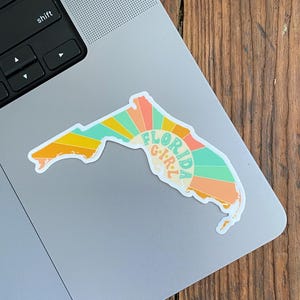 May include: A sticker of the state of Florida with a sunset design and the text "Florida Girl" in a retro font.