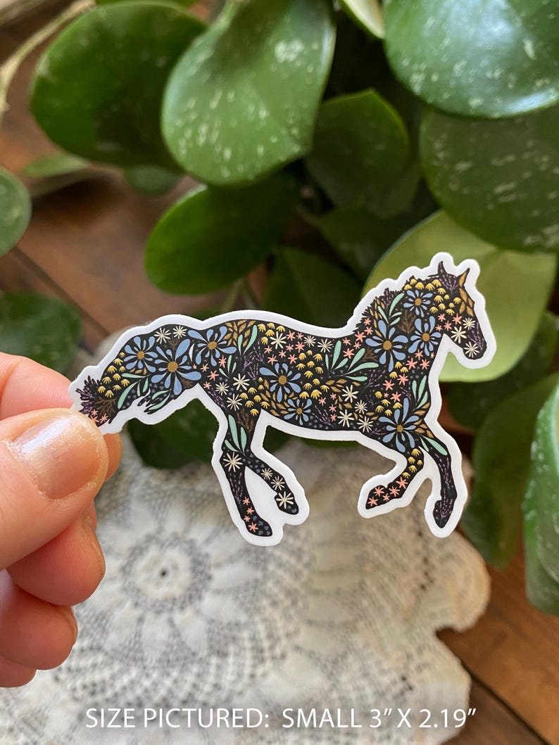 May include: A sticker of a horse in a running pose, decorated with a floral pattern in shades of blue, yellow, and pink on a black background. The sticker is approximately 3 inches by 2.19 inches.