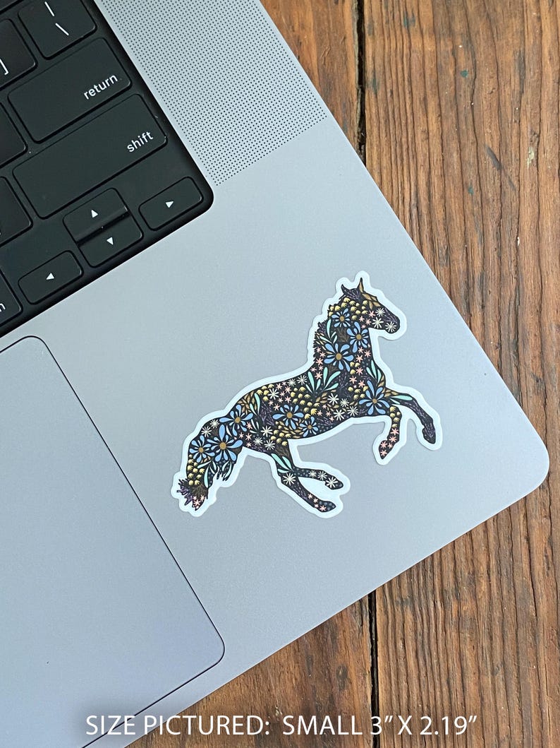 May include: A sticker of a horse in a running pose, decorated with a floral pattern in blue, white, and gold. The sticker is on a laptop. The text at the bottom reads: SIZE PICTURED: SMALL 3" X 2.19".