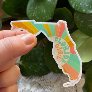 May include: A sticker of the state of Florida with a retro sunburst design and the text "Florida Girl" in a circle.