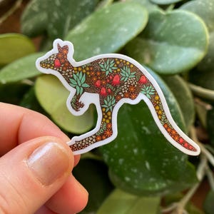 May include: A white sticker with a kangaroo silhouette outlined in a floral pattern. The pattern features green leaves, red flowers, and brown accents.