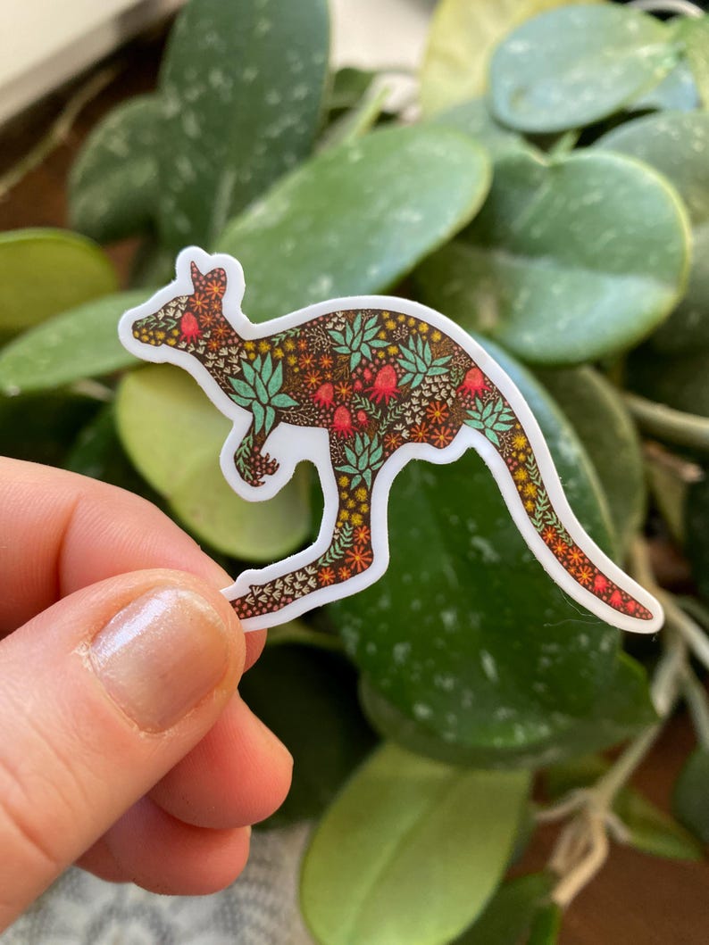 May include: A white sticker with a kangaroo silhouette outlined in a floral pattern. The pattern features green leaves, red flowers, and brown accents.