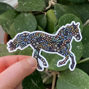 May include: A medium-sized sticker of a horse silhouette, adorned with a floral pattern in shades of blue, gold, pink, and white. The sticker measures 4 inches by 2.92 inches. The horse is set against a background of green foliage.