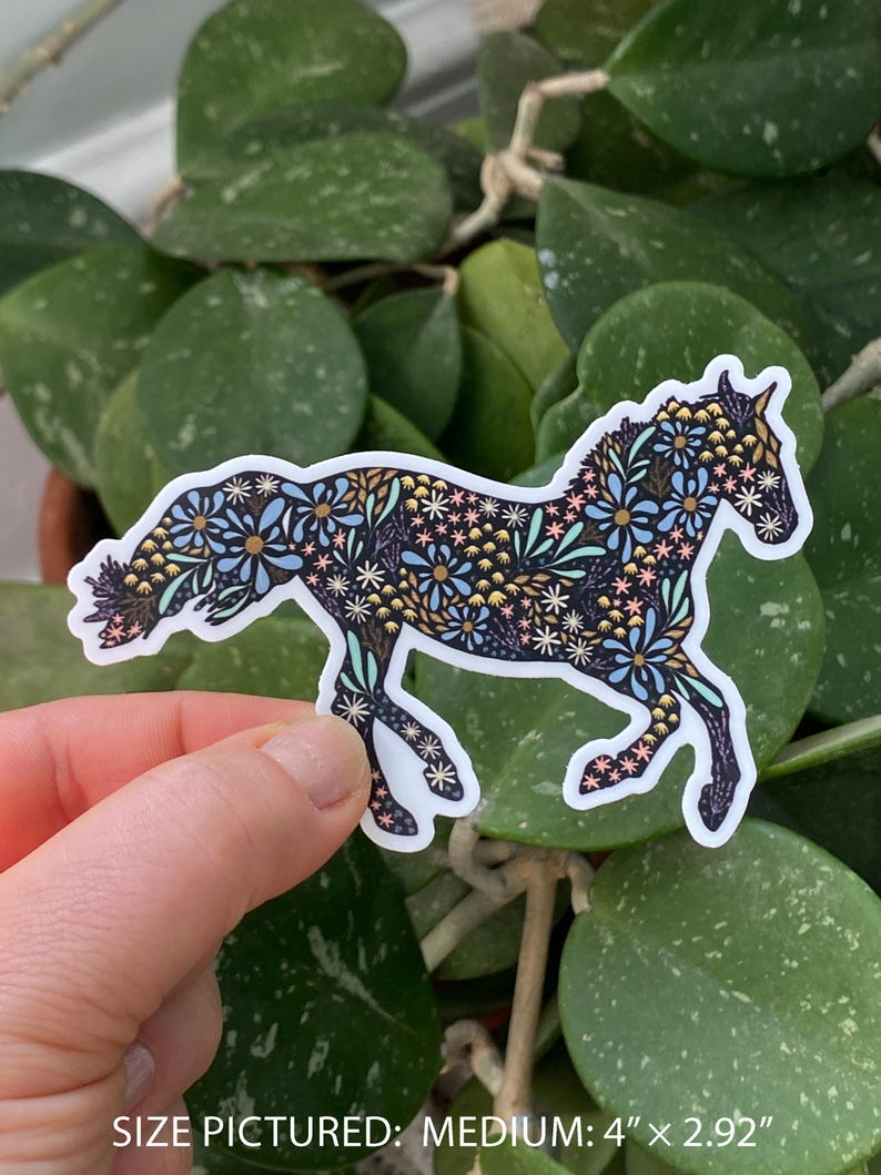 May include: A medium-sized sticker of a horse silhouette, adorned with a floral pattern in shades of blue, gold, pink, and white. The sticker measures 4 inches by 2.92 inches. The horse is set against a background of green foliage.