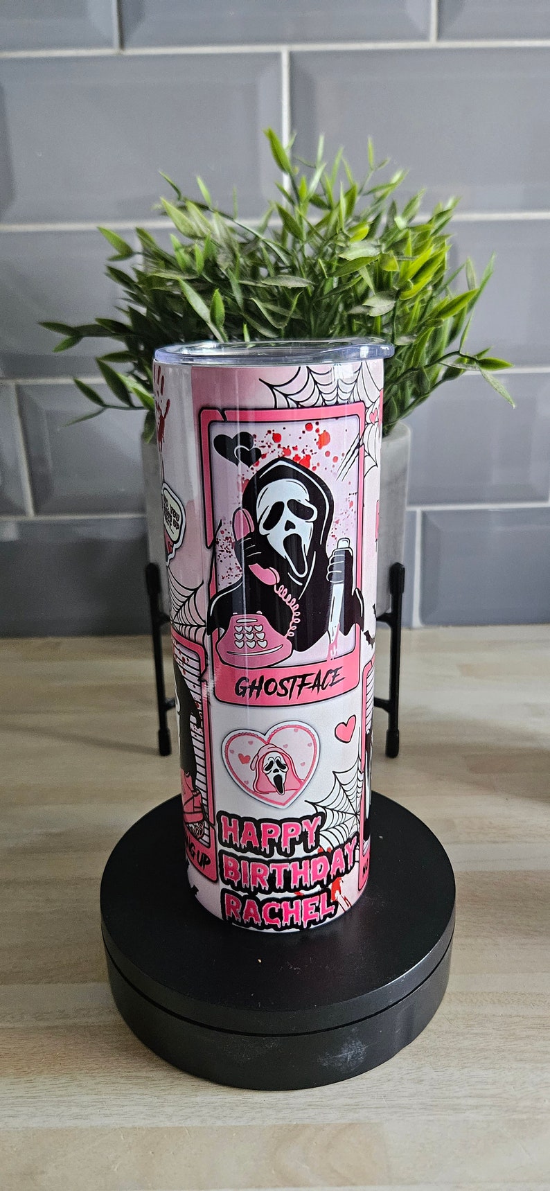 May include: Pink and black stainless steel tumbler with a graphic of Ghostface from the Scream movie franchise. The tumbler has a pink background with black spiderwebs and the text "Happy Birthday Rachel" and "Ghostface".