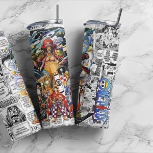 May include: Three stainless steel tumblers with lids and straws, featuring colorful manga-style artwork. The designs include characters and panels from a Japanese anime series. The tumblers are cylindrical and rest on a marble surface.