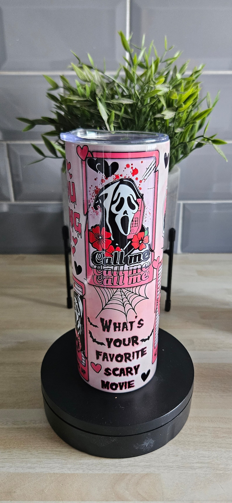 May include: Pink and black stainless steel tumbler with a graphic of a ghost wearing a mask and holding a phone. The text "Call me" is repeated three times. The text "What's your favorite scary movie" is also on the tumbler.