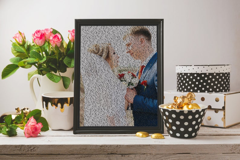 May include: A black framed photo of a wedding couple, with the image made up of tiny black dots. The photo is on a white shelf with a white pitcher, a white mug with gold dripping down the side, a pink rose, and a black and white polka dot bowl filled with gold chocolate candies.
