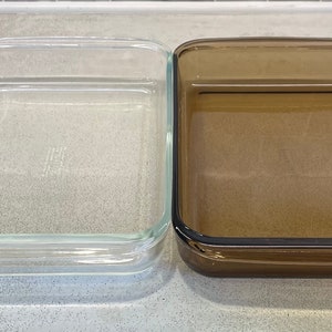 May include: Two rectangular glass baking dishes. One is clear, the other is a brown-tinted glass. Both have a simple, classic design with slightly rounded corners and a raised edge. Ideal for baking casseroles, desserts, or other dishes.